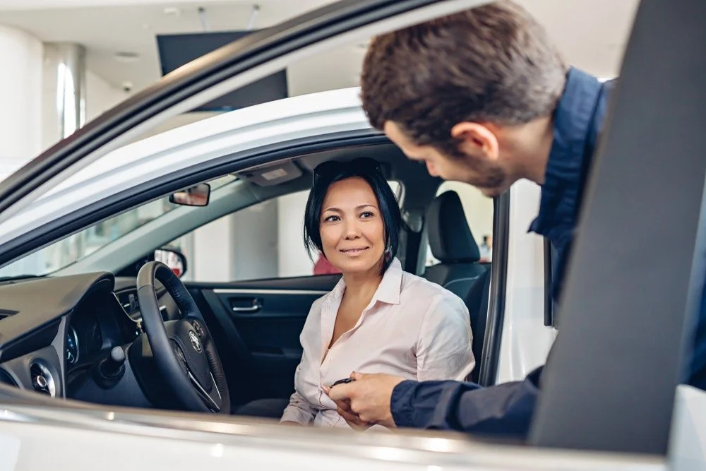 A dealership service advisor at a desk speaking on the phone while looking at a computer